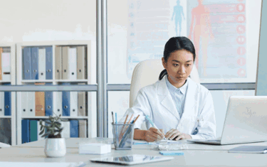 Image of a lady wearing a white coat working on her laptop