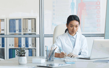 Image of a lady wearing a white coat working on her laptop